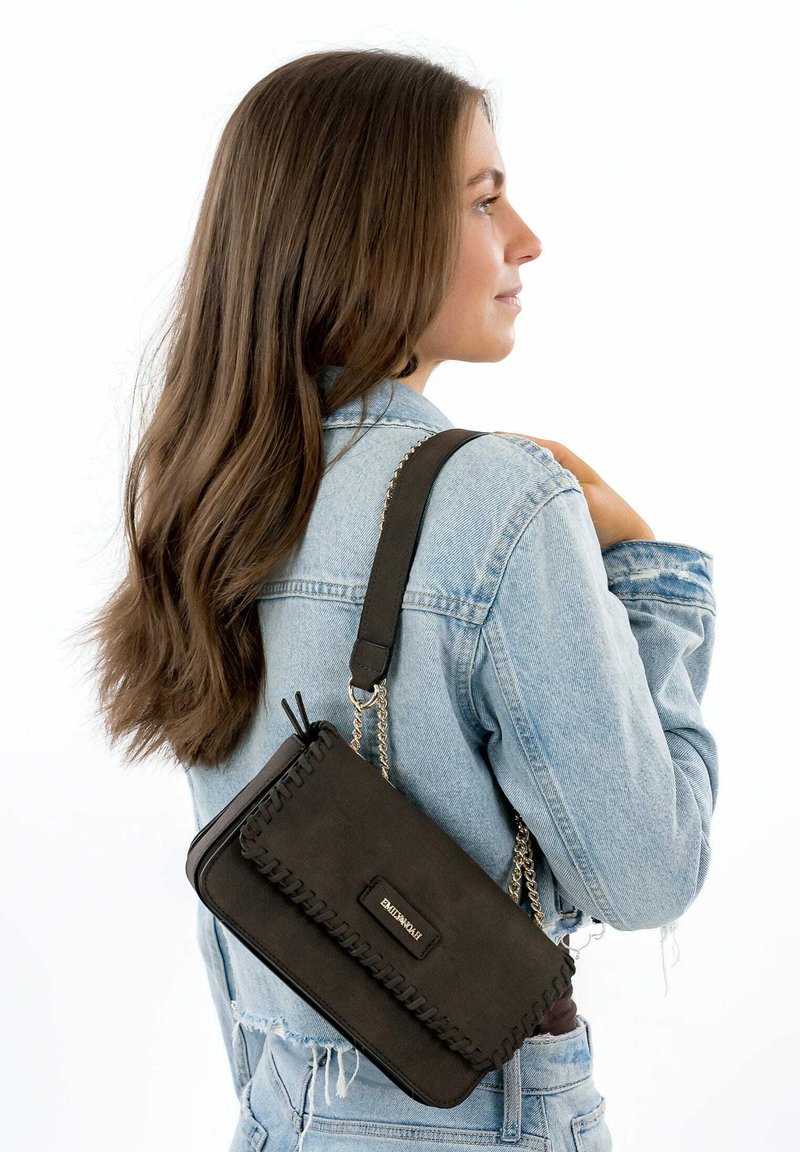 Sort læder crossbody taske med kædestrop, der har stygge kanter og en lille logo-plade. Tasken er rektangulær og tekstureret.