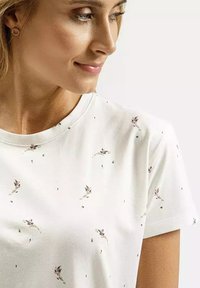 Biała koszulka z krótkim rękawem i okrągłym dekoltem, zdobiona rozsypanym kwiatowym wzorem w stonowanych kolorach na miękkim materiale.