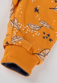 Orangefarbener Stoffärmel mit navyblauen Blatt- und Sternmustern, mit einem gerippten Bund und einer dunklen Innenseite.