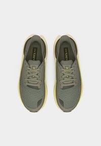 Ζευγάρι πράσινα και κίτρινα αθλητικά παπούτσια με κορδόνια, τοποθετημένα δίπλα-δίπλα πάνω σε λευκό φόντο.