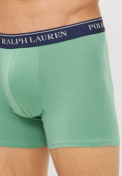 Zaļi kokvilnas bokseršorti ar tumši zilā josta, kurā ir "RALPH LAUREN" un "POLO" zīmoli. Gluda tekstūra un pieguloša dizaina.