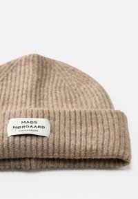 Bees värvitud kootud beanie müts ribakonstruktsiooniga ja volditud äärisega. Omab ristkülikukujulist silti, millel on musta värvi tekst "MADS NØRGAARD COPENHAGEN".