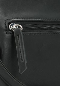 Detail van een zwarte leren tas met een zilveren rits en een trekband. Het oppervlak is glad met zichtbare stiksels en een subtiele textuur.