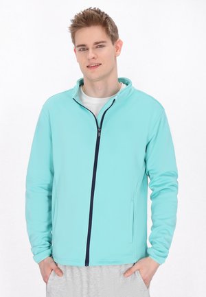 Lys blå zip-jakke med ståkrave, kontrasterende navy lynlås og sidelommer, lavet af glat stof velegnet til aktivt tøj.