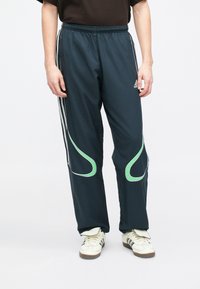 Tamsiai mėlyni sportiniai kelnaičiai su elastine juosmens juosta, kuriuose yra baltos šoninės juostelės ir žalios spiralinės detalės, pagaminti iš lengvos sintetinės medžiagos.