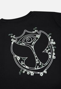Zwarte t-shirt met een groot wit geborduurd embleem met bloemenaccenten in groen en wit, met complexe patronen en details.
