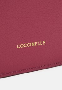Portafoglio in pelle magenta con superficie testurizzata, dotato di logo 'COCCINELLE' in rilievo dorato e dettagli di cucitura in contrasto.