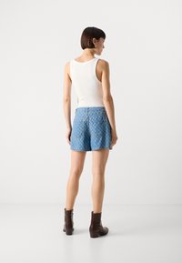 Denim šorti ar gaiši zilā krāsā, ar dimanta rakstu un aizmugurējām kabatām, apvienoti ar bez piedurknēm baltu topu un brūnām potītēm zābakiem.
