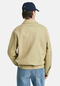 Beige overshirt med afslappet pasform, krave, elastisk kant og knapmanchetter, parret med lyseblå denim jeans.