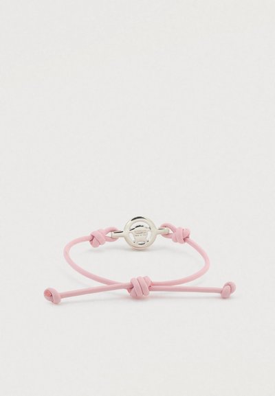 Rožinė reguliuojama apyrankė iš lygaus odos su sidabro spalvos apvaliu užsegimu ir mazgais iš abiejų pusių.