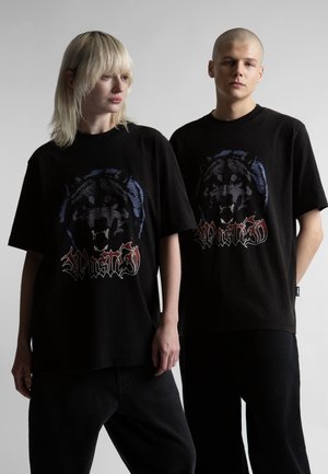 Două persoane purtând tricouri negre supradimensionate cu un lup care mârâie și textul „Wasted”, stând în fața unui fundal gri simplu.