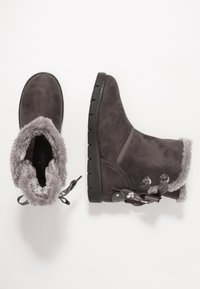 Botas de ante gris hasta el tobillo con forro de piel sintética, puntera redonda, suela de goma negra flexible y adornos de cinta decorativa a los lados.