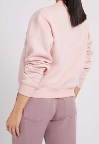 Sudadera rosa claro con cuello redondo, puños y dobladillo de canalé. Combinada con pantalones rosa claro a juego que cuentan con bolsillos traseros.