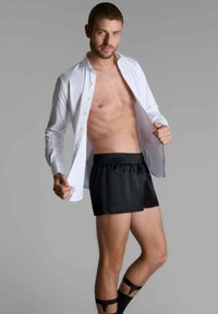 Chemise blanche à boutonnage, décolletée, associée à un short en satin noir. Caractéristiques : ceinture élastique et fentes latérales pour plus de liberté de mouvement.