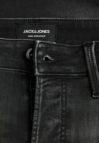 Jeans de mezclilla negra con una textura ligeramente deslavada, que presentan un cierre de botón y cremallera, costuras reforzadas y una etiqueta de marca prominente.