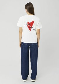T-shirt en coton blanc arborant un graphique de grand cœur rouge vif avec le texte « J'AIME NEW YORK » en noir, associé à un jean en denim foncé à jambes larges.