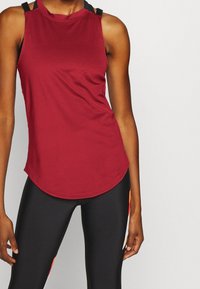 Bourgondische mouwloze sporttop met afgeronde zoom, contrasterende zwarte banddetails op de schouders en glad, lichtgewicht materiaal.