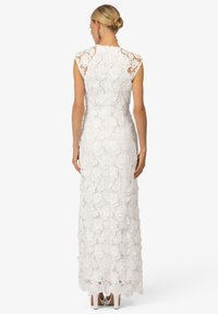 Abito bianco in pizzo con silhouette aderente, maniche a kimono e motivo floreale. La schiena presenta una cerniera nascosta e una leggera strascico.