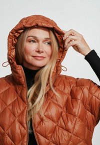 Puchowy brązowy kurtka z kapturem, z zapięciem na zamek i sznurkami do regulacji. Gładka, błyszcząca tekstura z diamentowymi wzorami.