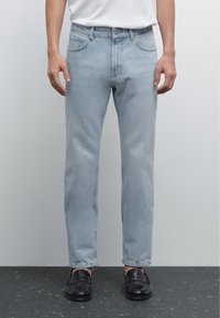 Light blue straight-leg denim jeans with a classic five-pocket design and a slight fade, paired with black loafers.