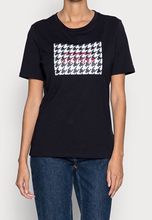 Sort kortærmet t-shirt i bomuld med et rektangulært hvidt og marineblåt hundetandsmønster og teksten 'TOMMY HILFIGER' i pink.