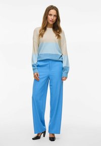 Sweter w blokach kolorystycznych z beżowymi i niebieskimi paskami, zestawiony z luźnymi niebieskimi spodniami. Całość dopełniają czarne szpilki.