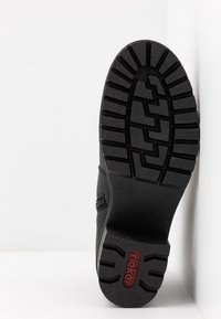 Suela de zapato negra con superficie de goma texturizada y patrón de banda de rodadura en zigzag; presenta un logo elevado y una impresión de tamaño en el talón.