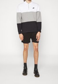 Nike kvartdraget tröja, färgblockerad i vitt, grått och svart. Har lång ärm och en svart krage. Bärs med svarta shorts och stövlar.