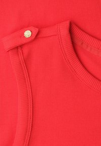 Gros plan d'un vêtement en tissu côtelé rouge avec un col rond et un petit bouton doré sur une bretelle.