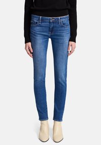 Jeans skinny blu realizzati in denim, dotati di cinque tasche, chiusura con bottone e leggera scoloritura. Abbinati a stivali alla caviglia beige.