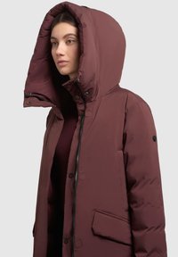 Bordowa kurtka puchowa z dużym kapturem, przednim zamkiem, zatrzaskami i bocznymi kieszeniami; gładki, błyszczący materiał i ocieplana konstrukcja.