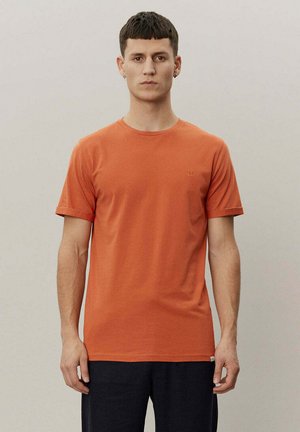 Kortermet oransje T-skjorte laget av bomull med rund hals og en liten brodert detalj på brystet, med en glatt tekstur.