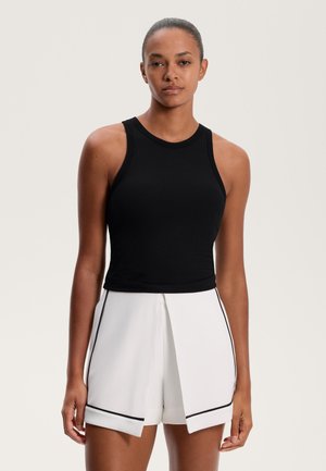 Black ribbed tank top with a fitted design, paired with white shorts featuring a split front and black trim. Smooth textures throughout.