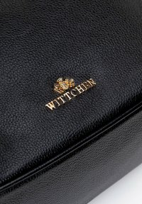 Czarna skórzana torebka o teksturowanym wykończeniu. Posiada złote logo i emblemat z przodu, z prostymi liniami i wyraźnie zarysowanym kształtem.