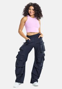 Kitsas roosa crop-top ilma varrukateta disainiga, millele on lisatud laiad tumesinised cargo-püksid suurte volangidega ja mitme taskuga. Valged tossud.