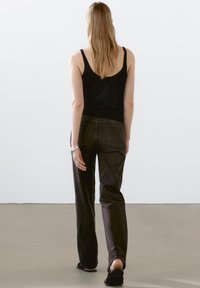 Svart linne, mörkgrå jeans, avslappnad passform. Enkelt design, minimal detaljering, slät textur. Barfota med flata sandaler; neutral bakgrund.