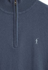 Blå stickad tröja med halvdragkedja vid kragen. Har en ribbad halsringning och en liten broderad golfspelare i ljusblått på bröstet.