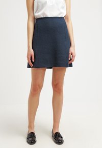 Una gonna A-line blu scuro realizzata in tessuto testurizzato, con vita alta e linee pulite, abbinata a scarpe dress nere.