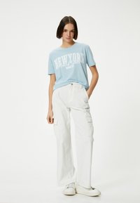 Camiseta de algodón azul clara con la impresión "NUEVA YORK Estados Unidos", combinada con pantalones cargo blancos de corte holgado con bolsillos laterales. Zapatillas blancas.