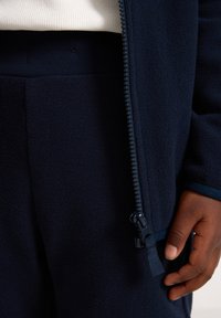 Navy fleece jacket with a zip closure, featuring a soft texture and contrasting zip detail, paired with matching navy pants.