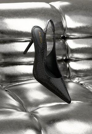 Black crocodile-texture slingback high heel shoe with pointed toe on shiny silver tufted surface.