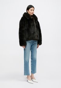 Σκούρο καφέ μπουφάν από ψεύτικη γούνα με φαρδιά γιακά, φορεμένο πάνω από ανοιχτό μπλε τζιν με ίσια γραμμή και άσπρα γαλοτσάκια με μύτη σε σχήμα βέλους. Λείος υφάσματος.