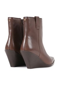 Botas de tobillo de cuña de cuero marrón con un acabado suave, punta afilada y detalles de costura vertical. Presentan un elegante tacón de cuña y sutiles acentos de hardware.