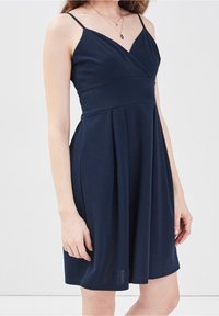 Vestido sin mangas de color azul marino con escote en V, corpiño ajustado y falda plisada. Hecho de una tela suave con finas tirantes tipo espagueti.