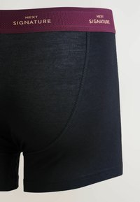 Sötét tengerészkék boxeralsó texturált lila derékrésszel, amelyen arany betűkkel "NEXT" és "SIGNATURE" felirat látható. Simább anyag, varrási részletekkel.