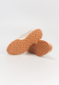 Beżowe buty sportowe z teksturowaną gumową podeszwą, z gładką cholewką i delikatnymi akcentami oraz minimalistycznym wzornictwem.