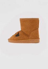 Brun mockason kort stövel med rund tå, med svarta broderade detaljer som liknar en hunds ansikte. Platt gummisula med förstärkt söm.