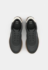 Scarpe sportive nere con una texture liscia, dotate di un accento crema sul tallone e una suola in gomma marrone. Lacci e marchio sulla linguetta.