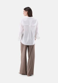 Camicia bianca a pois con maniche lunghe e dettaglio dello spacco posteriore, abbinata a pantaloni larghi di colore marrone chiaro.