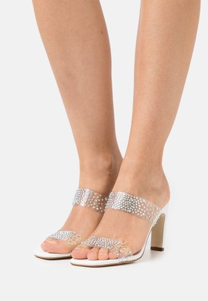 Sandales à talons transparents avec deux brides transparentes ornées de strass étincelants. Présente une semelle blanche et un design à bout ouvert.